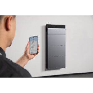 Man bedient Anker SOLIX thuisbatterij via smartphone-app, gemonteerd aan de muur voor ruimtebesparende energieopslag en monitoring.